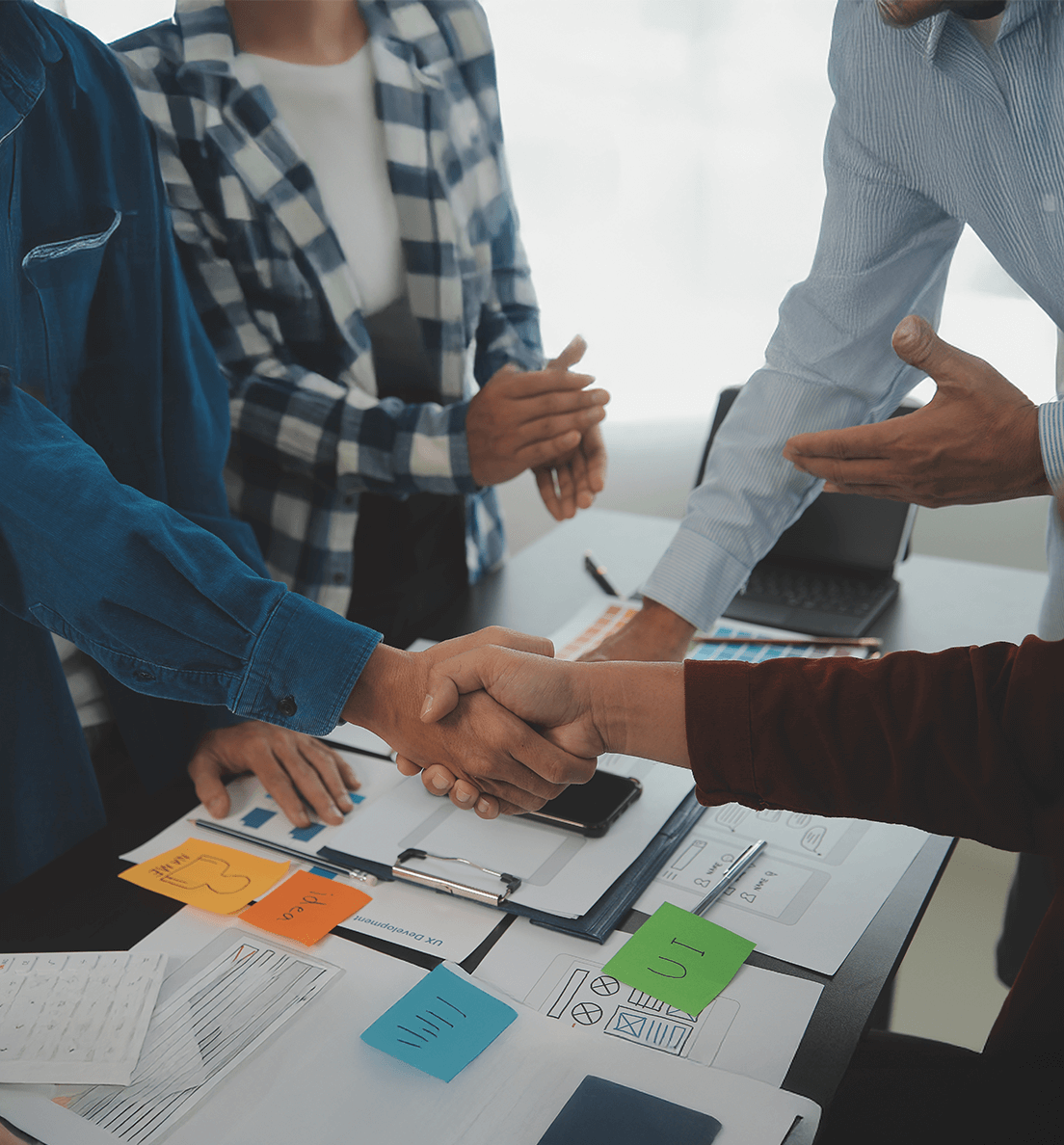 Team members collaborating around a table and shaking hands to represent value realization and business alignment.